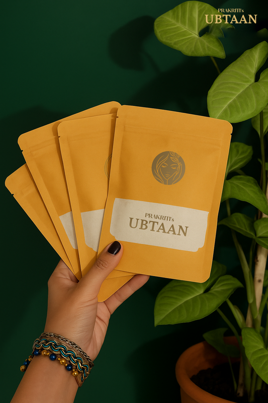 Hand holding yellow packages with 'Ubtaan' Organic Face Pack branding against a green background 